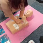 Participant performing chest compressions on an adult CPR manikin as part of emergency first aid training.