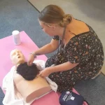 Learner preparing an adult CPR manikin by removing chest hair during AED training.