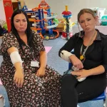Two participants sitting and demonstrating arm bandaging techniques during a first aid class.