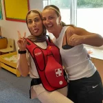 Two participants posing together while demonstrating a choking‑vest training aid.