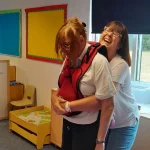 A learner practising abdominal thrusts on a choking‑vest training aid.