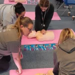 Group practising CPR techniques together on training manikins during a first aid workshop.