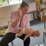 A first aid learner practising the back blow technique for infant choking relief using a specialized baby manikin.
