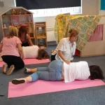 Adults practicing the recovery position during a first aid training session in a classroom, with pairs working on mats to learn emergency response skills.
